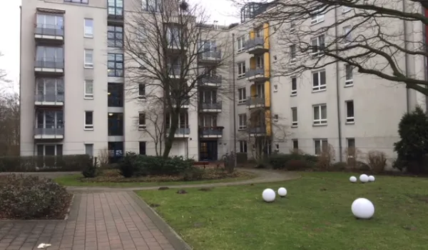 Moderne Wohnanlage mit mehreren mehrstöckigen Gebäuden in hellen Farbtönen. Gepflegte Außenanlage mit Rasenfläche, dekorativen weißen Kugeln und gepflasterten Wegen zwischen den Häusern.