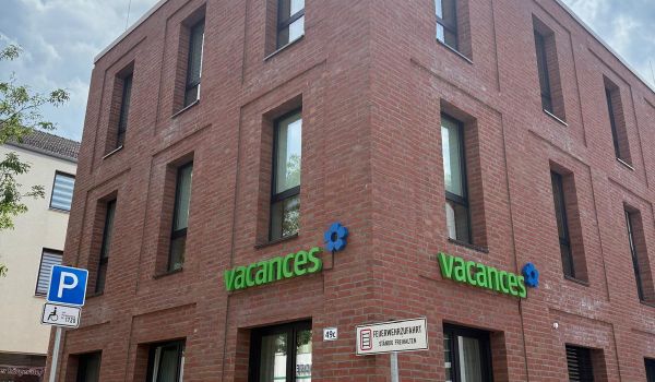 Modernes zweigeschossiges Backsteingebäude Tagespflege Bremen Vegesack mit grünen vacances-Logo. Zeitgemäße Architektur mit großen Fenstern und gepflastertem Vorplatz.