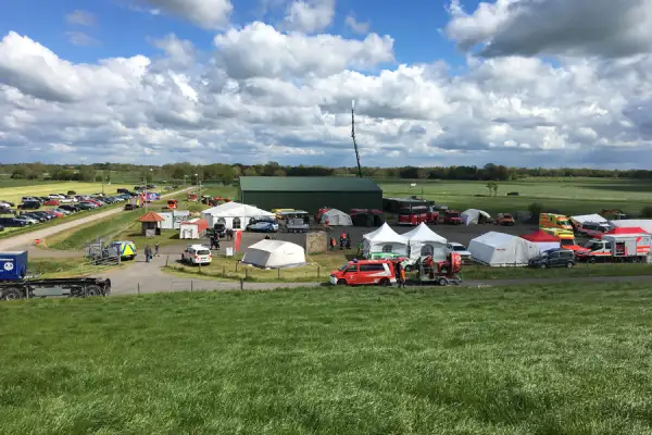 Veranstaltungsgelände mit Zelten und Fahrzeugen auf ländlicher Wiese unter dramatischem Wolkenhimmel.