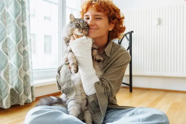 Junge Frau mit Gipsarm hält lächelnd ihre Katze im Arm – Symbolbild für Unterstützung im Alltag nach einem Krankenhausaufenthalt, unabhängig vom Alter.