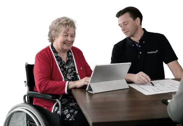 Pflegeberater von vacances zeigt einer Frau im Rollstuhl einen Grundriss und erklärt Maßnahmen am Tablet – Symbolbild für die Beratung zur Wohnraumanpassung.