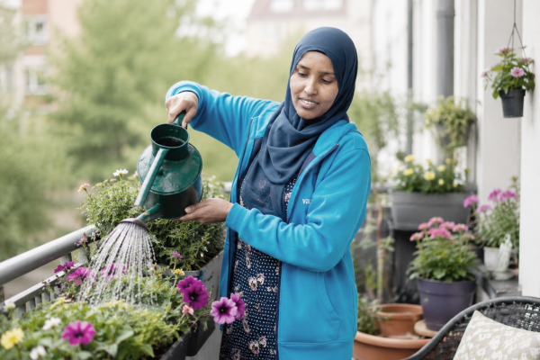 Alltagshelferin von vacances gießt lächelnd bunte Balkonblumen mit einer grünen Gießkanne.
